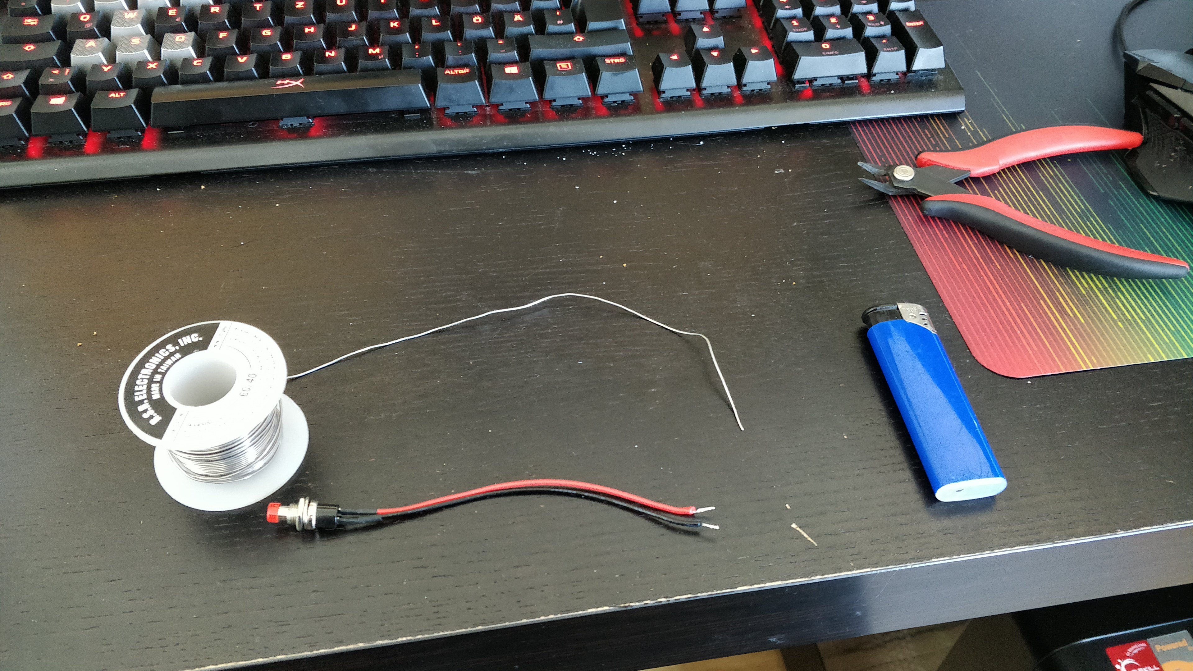 A desk with a wire cutter, a spool of solder, a button and a lighter